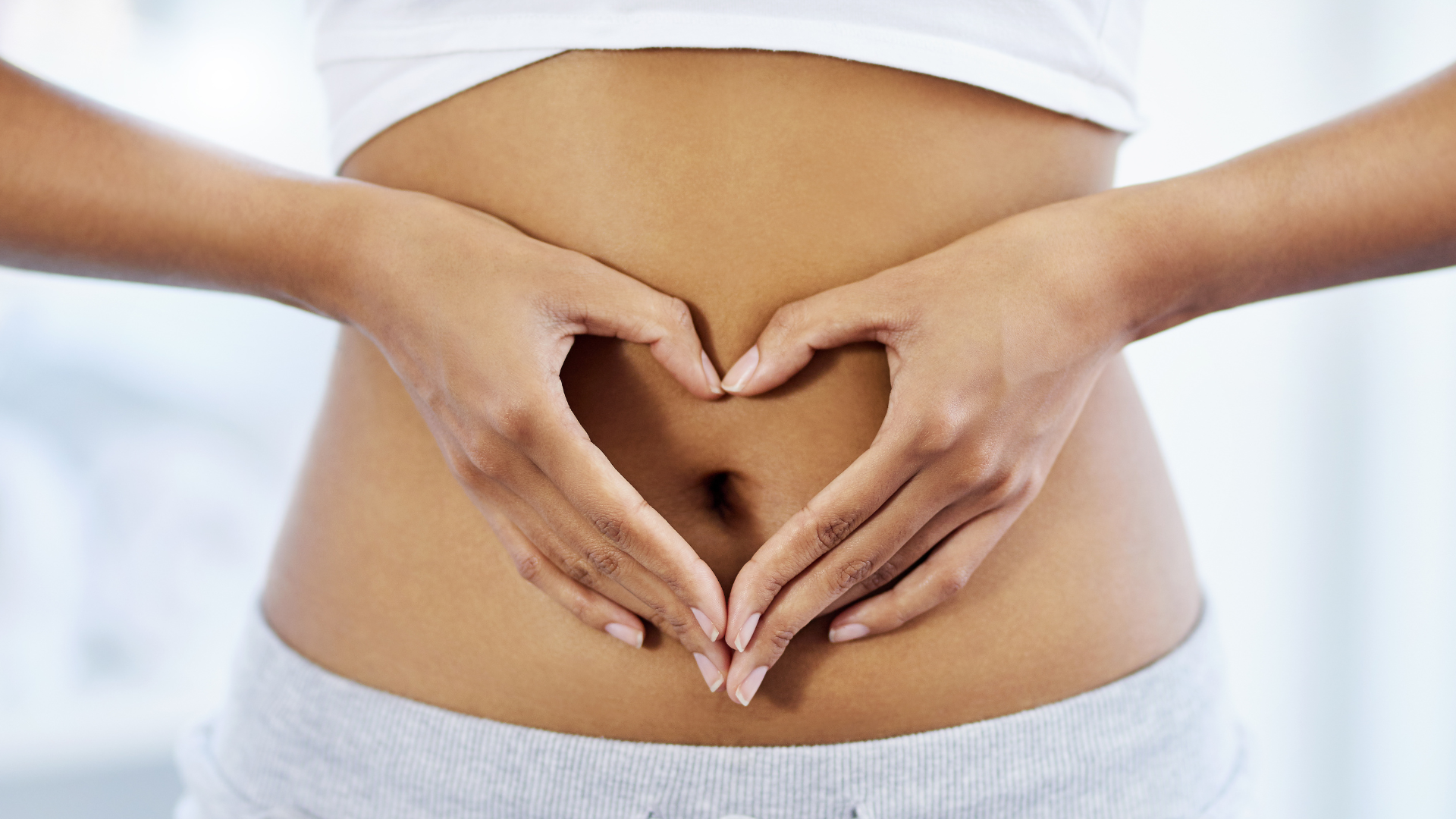 Žena koja radi oblik srca dlanovima ispred trbuha, simbolizirajući zdravlje crijeva